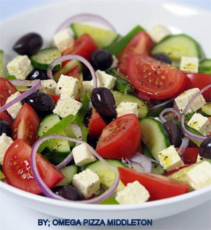 Fresh Greek salad with tomatoes, cucumbers, black olives, feta cheese cubes, and red onion rings.
