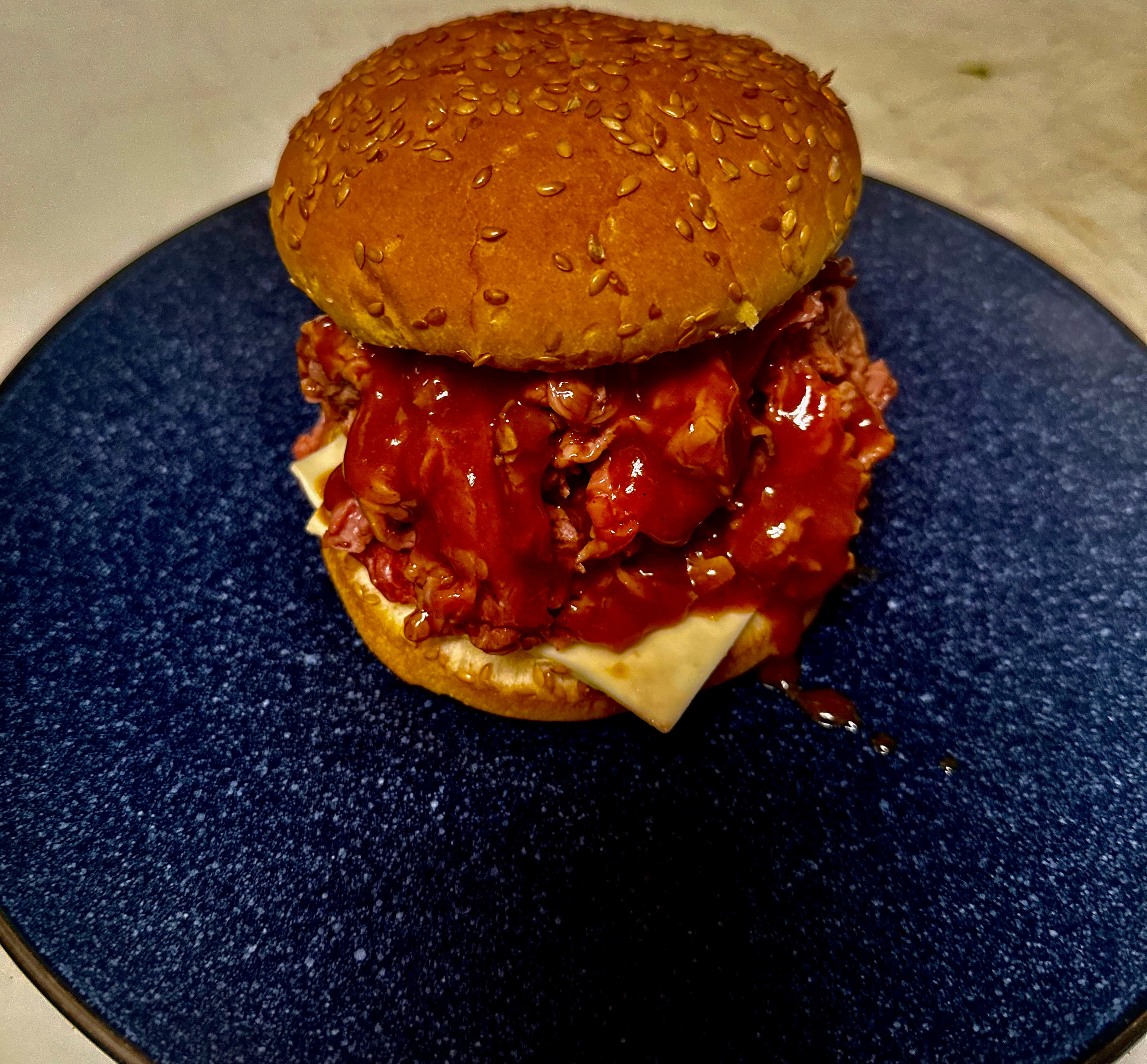 Roast beef sandwich with dripping red sauce and cheese on a sesame seed bun.