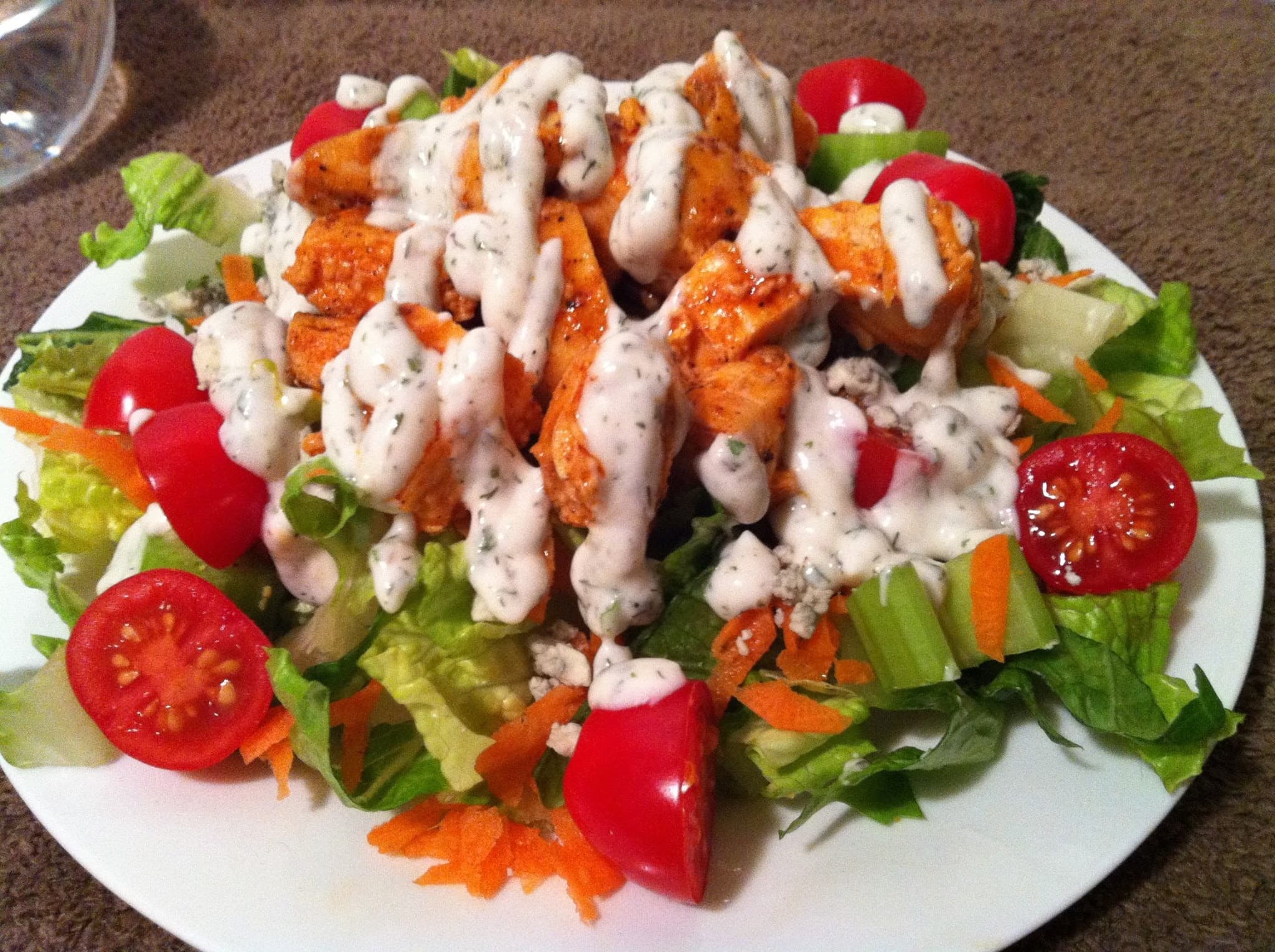 Buffalo chicken salad with cherry tomatoes, carrots, and celery, topped with creamy ranch dressing.