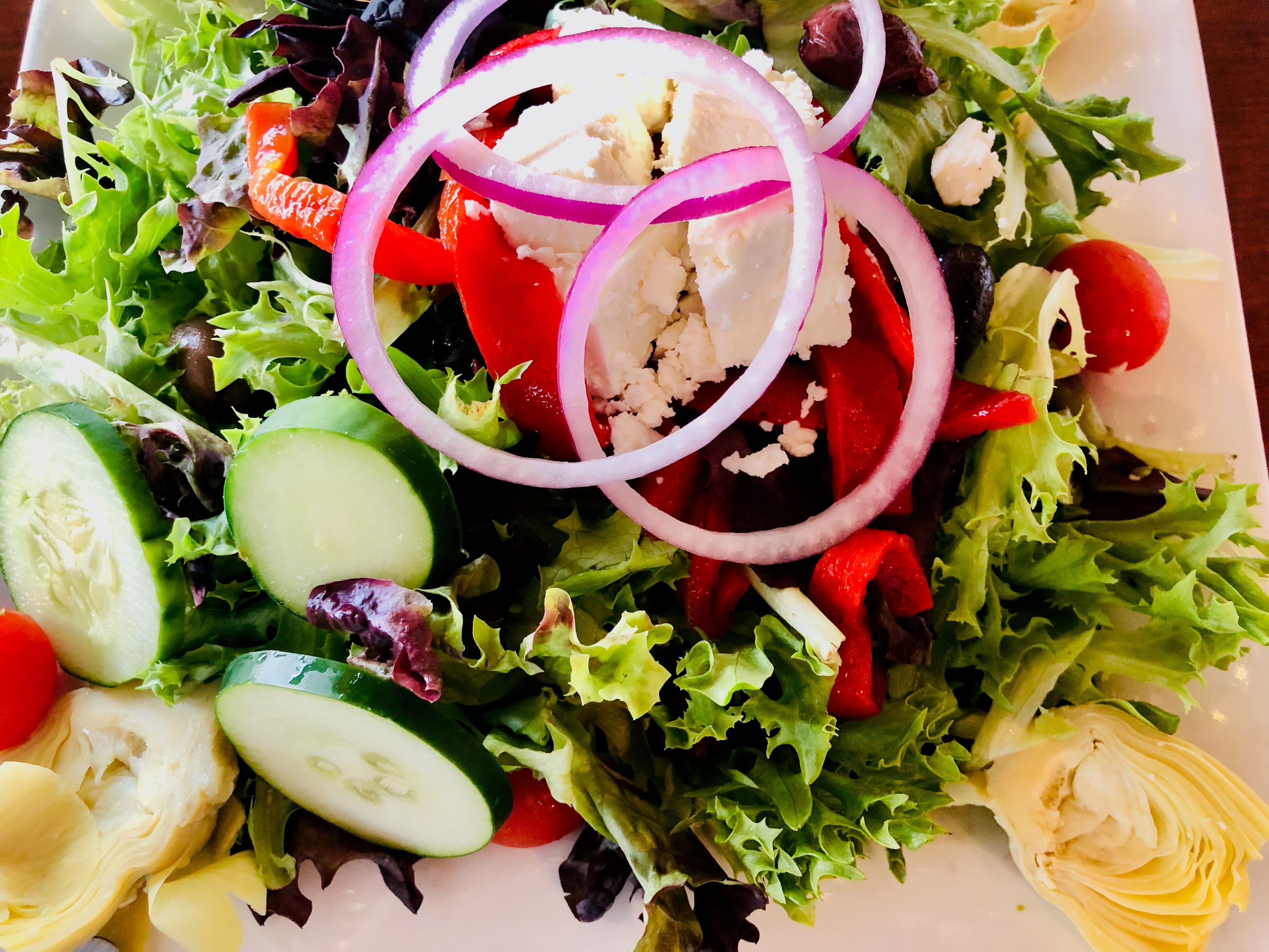 Fresh Greek salad with mixed greens, cucumber, red onion, feta cheese, peppers, and artichokes.
